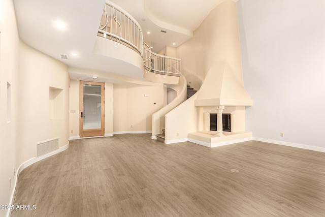 unfurnished living room featuring hardwood / wood-style floors, a towering ceiling, and a large fireplace