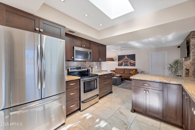 kitchen featuring a skylight, decorative backsplash, dark brown cabinetry, light stone counters, and stainless steel appliances