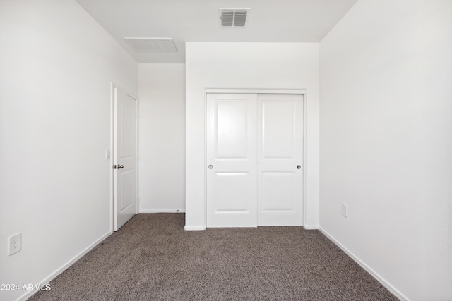 unfurnished bedroom with dark carpet and a closet