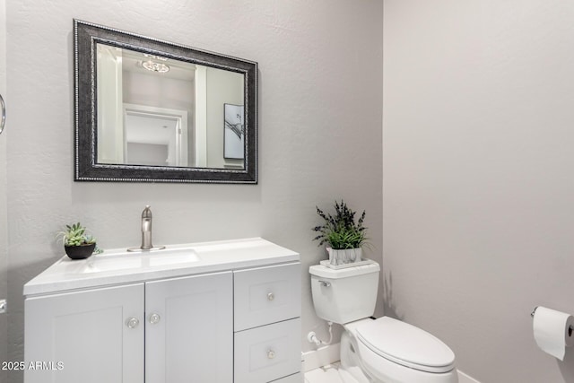 half bath with baseboards, vanity, and toilet