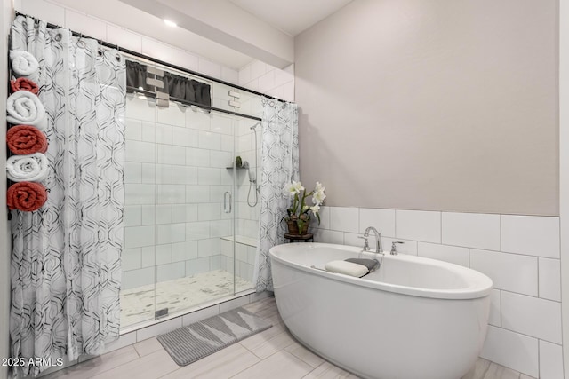 full bath featuring a wainscoted wall, a freestanding tub, a shower stall, and tile walls