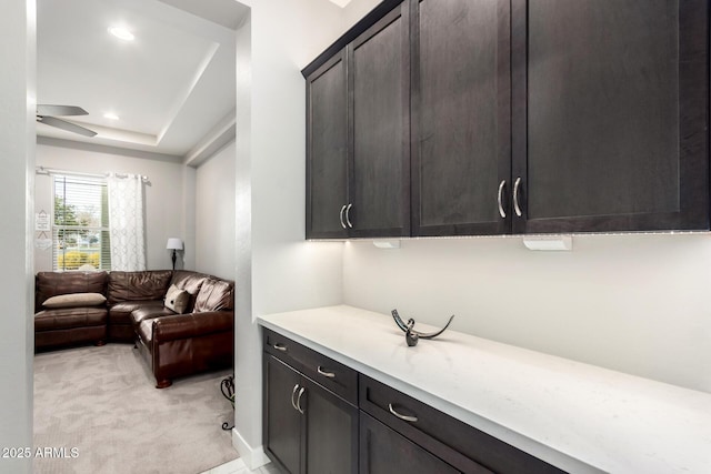 interior space featuring a raised ceiling, light colored carpet, ceiling fan, light countertops, and recessed lighting