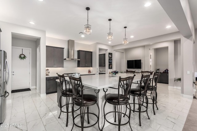 kitchen featuring marble finish floor, wall chimney exhaust hood, light countertops, and recessed lighting