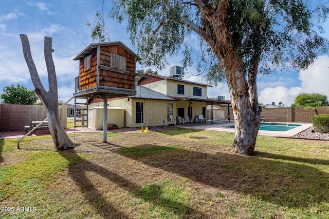 rear view of property with cooling unit, a shed, a yard, and a fenced in pool