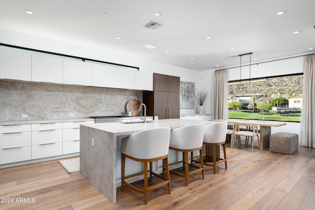 kitchen with a kitchen bar, sink, a center island with sink, white cabinets, and light hardwood / wood-style floors