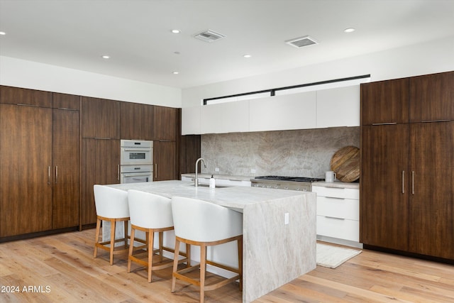 kitchen featuring white cabinetry, sink, an island with sink, and light hardwood / wood-style floors