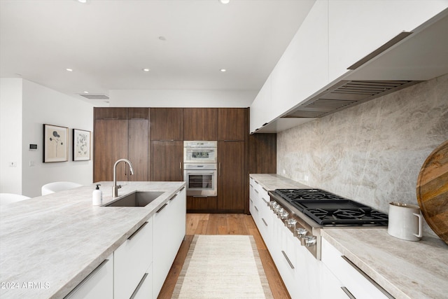 kitchen featuring light wood-type flooring, dark brown cabinets, double oven, sink, and white cabinetry