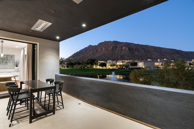 balcony at dusk featuring a water and mountain view