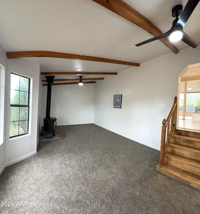 unfurnished living room with a healthy amount of sunlight, beam ceiling, ceiling fan, and a wood stove