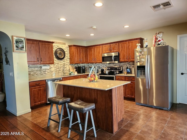 kitchen featuring a kitchen island, appliances with stainless steel finishes, a breakfast bar, sink, and backsplash