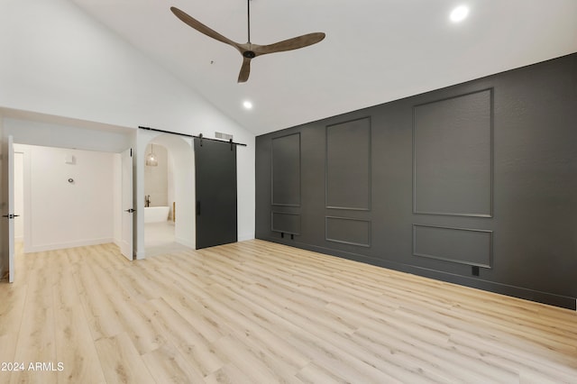 unfurnished bedroom with ceiling fan, a barn door, high vaulted ceiling, connected bathroom, and light hardwood / wood-style floors