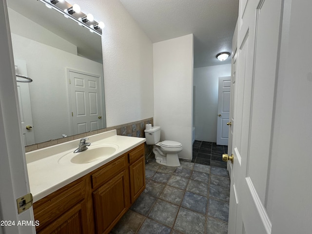 bathroom with a textured ceiling, vanity, toilet, and tile flooring