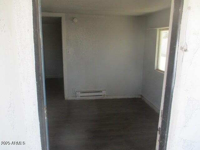 unfurnished room with baseboard heating, wood finished floors, and baseboards