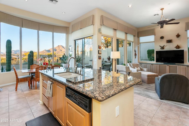 kitchen with sink, dark stone countertops, light tile patterned floors, and an island with sink