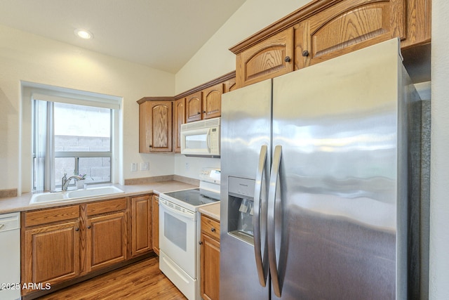 kitchen with a sink, white appliances, light wood-style floors, light countertops, and lofted ceiling