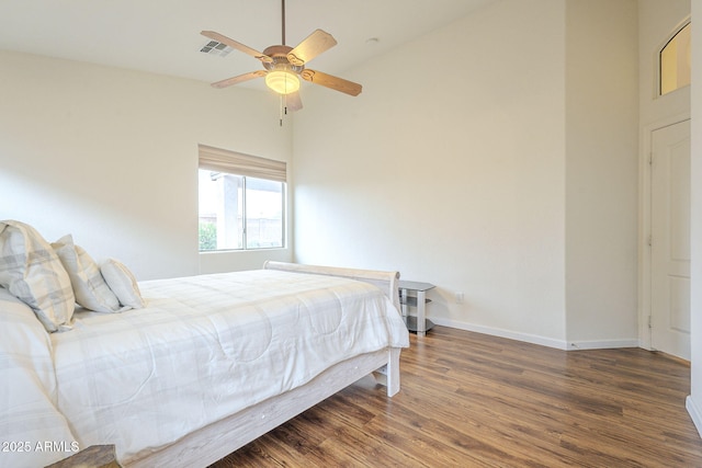 bedroom featuring visible vents, wood finished floors, a high ceiling, baseboards, and ceiling fan