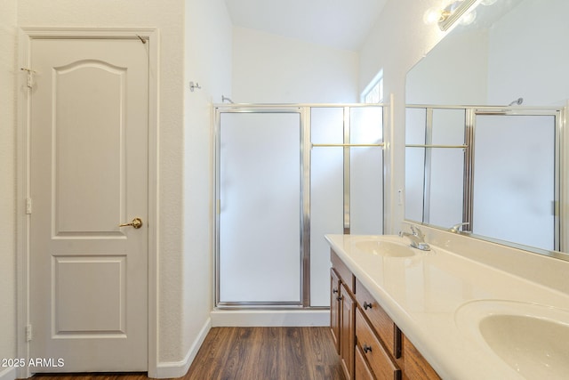 bathroom with a stall shower, a sink, wood finished floors, double vanity, and vaulted ceiling