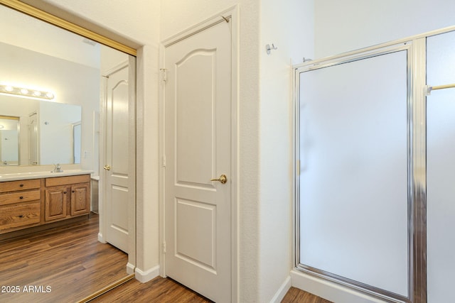 bathroom featuring vanity, wood finished floors, baseboards, and a shower with door