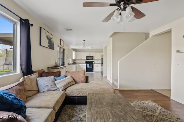 living area with light wood-type flooring, baseboards, visible vents, and ceiling fan