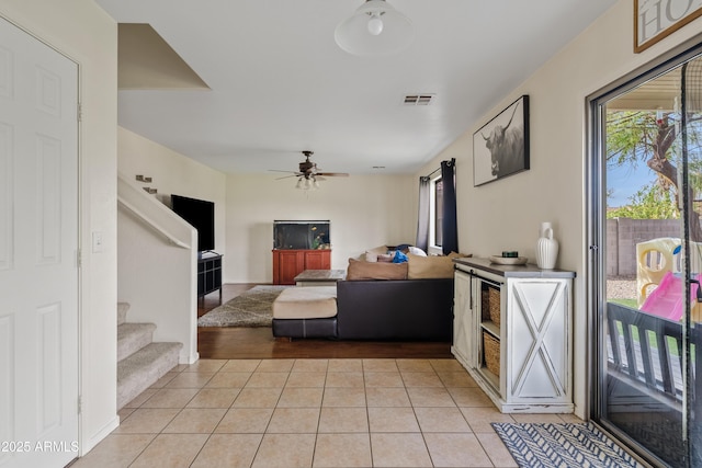 living area with light tile patterned floors, visible vents, ceiling fan, and stairs