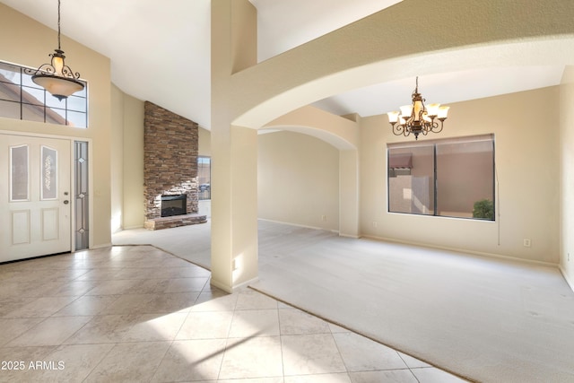 carpeted entrance foyer with a stone fireplace, a healthy amount of sunlight, a notable chandelier, and high vaulted ceiling