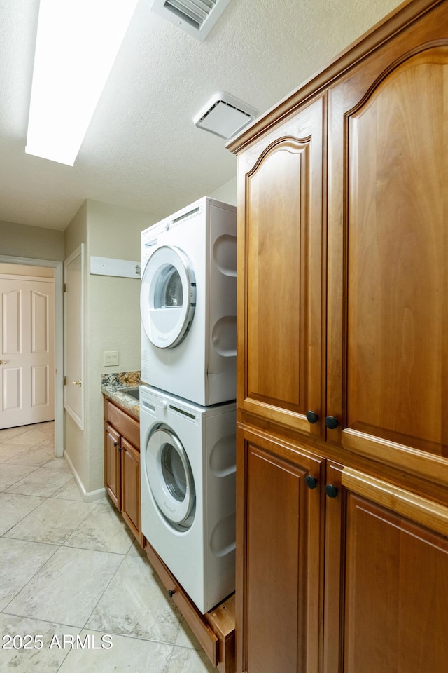 washroom featuring a skylight, cabinets, and stacked washer / dryer