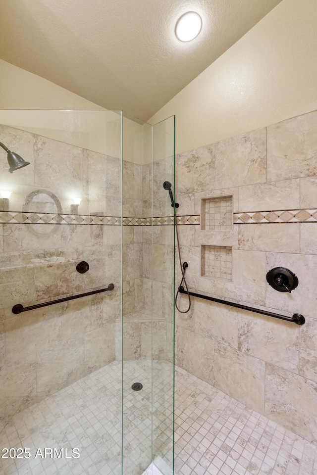 bathroom featuring vaulted ceiling, a textured ceiling, and a tile shower