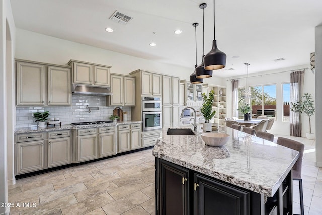 kitchen with sink, a breakfast bar area, a kitchen island with sink, hanging light fixtures, and decorative backsplash