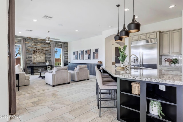 kitchen featuring stainless steel built in refrigerator, light stone counters, decorative light fixtures, cream cabinets, and backsplash