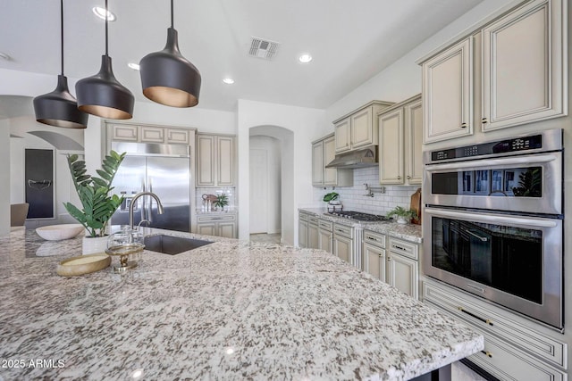 kitchen with cream cabinets, appliances with stainless steel finishes, sink, and light stone counters