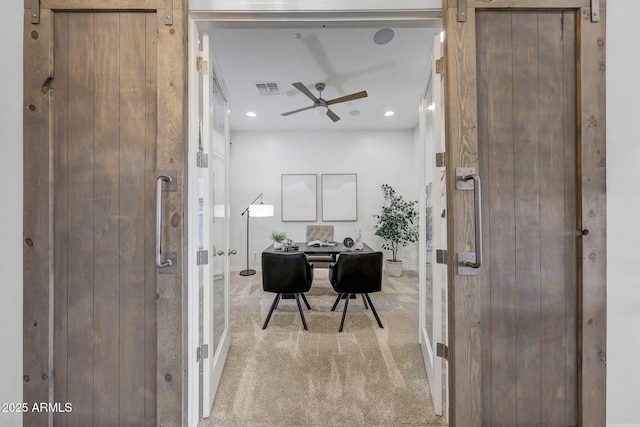 office with a barn door, light carpet, and ceiling fan