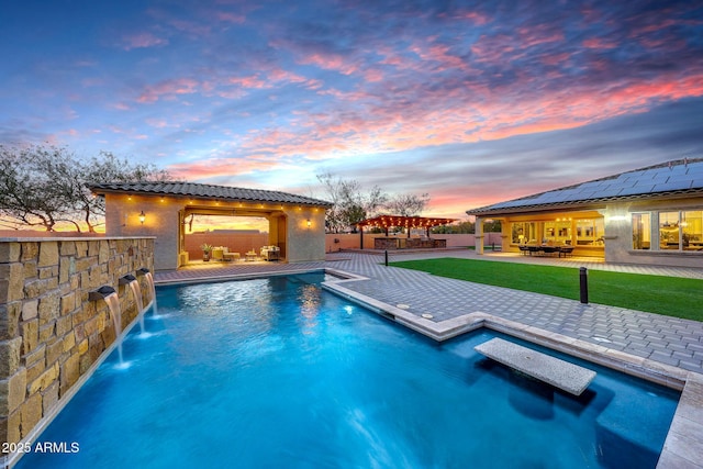 pool at dusk with a lawn, a patio, and pool water feature