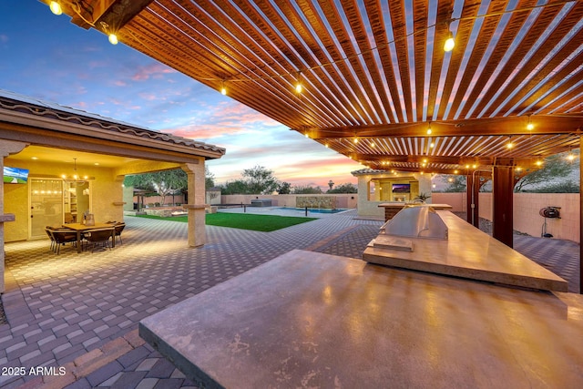 patio terrace at dusk with area for grilling and a pergola