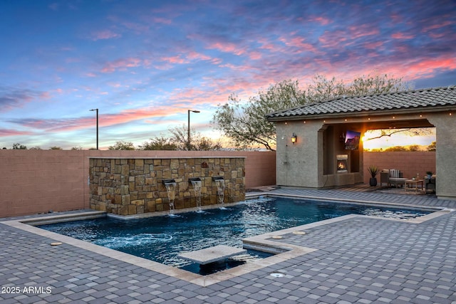 pool at dusk with pool water feature and a patio area