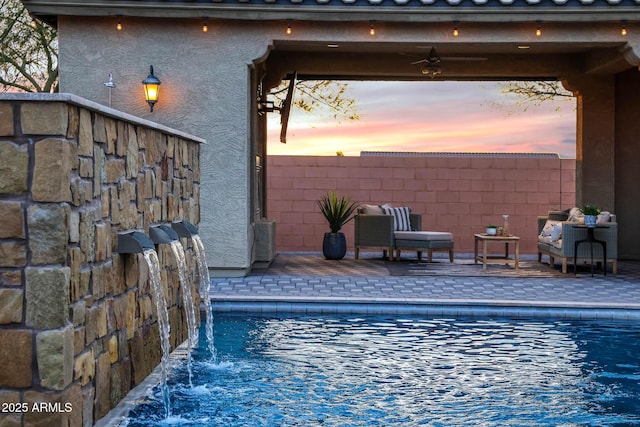 pool at dusk featuring a patio, pool water feature, and ceiling fan