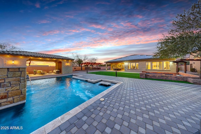 pool at dusk featuring pool water feature and a patio area