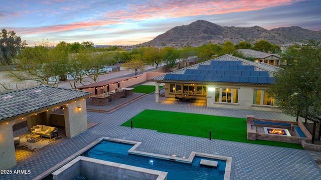 back house at dusk featuring a mountain view, a lawn, an outdoor living space with a fire pit, and a patio