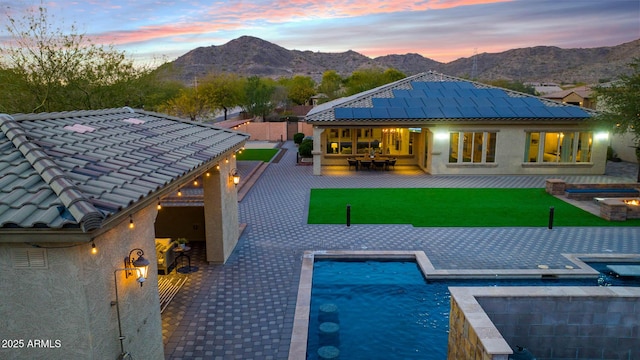 back house at dusk featuring a mountain view, a yard, and a patio area