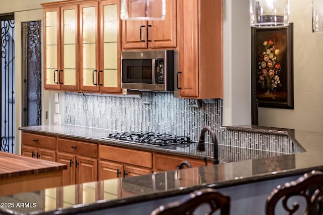 kitchen with tasteful backsplash, brown cabinetry, appliances with stainless steel finishes, and glass insert cabinets