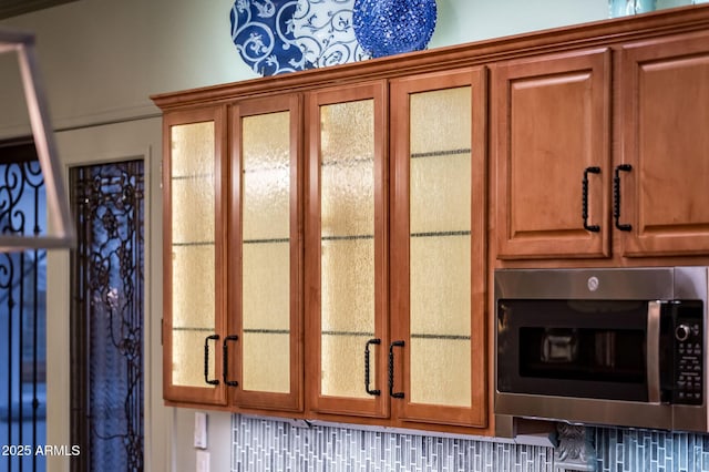 room details with brown cabinetry, stainless steel microwave, and glass insert cabinets