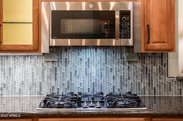 room details featuring stainless steel microwave, decorative backsplash, and black gas stovetop