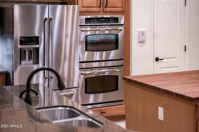 kitchen with a sink, brown cabinetry, appliances with stainless steel finishes, and butcher block countertops