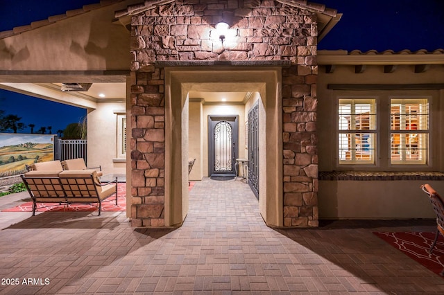 exterior entry at night featuring stucco siding and stone siding