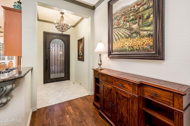 foyer entrance featuring an inviting chandelier, crown molding, wood finished floors, and baseboards