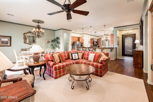 living room featuring visible vents, baseboards, dark wood finished floors, ornamental molding, and ceiling fan with notable chandelier