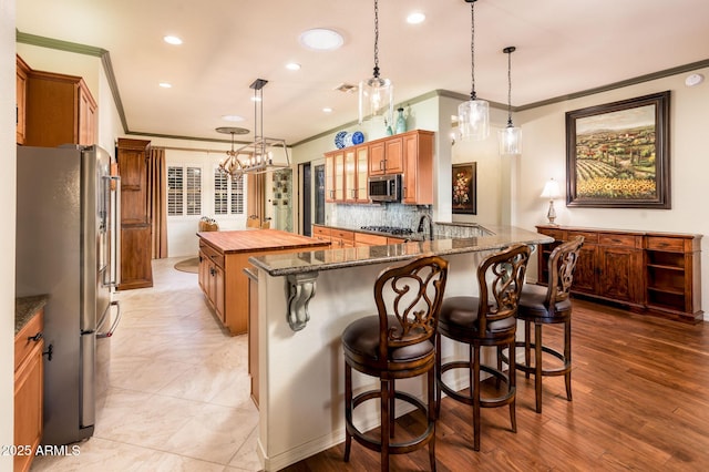 kitchen with a breakfast bar, ornamental molding, tasteful backsplash, dark stone counters, and appliances with stainless steel finishes