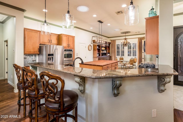 kitchen with visible vents, crown molding, dark wood-type flooring, a breakfast bar, and appliances with stainless steel finishes