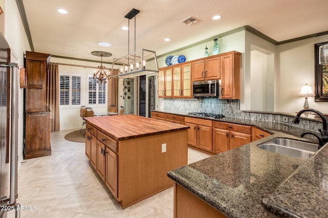 kitchen featuring a kitchen island, crown molding, butcher block countertops, appliances with stainless steel finishes, and a sink