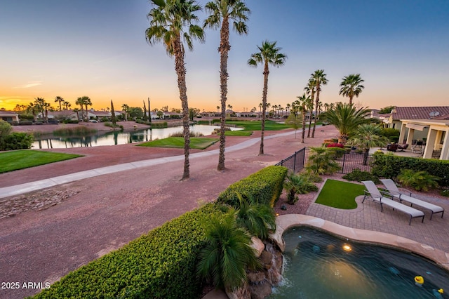 pool at dusk with a patio area, fence, and a water view