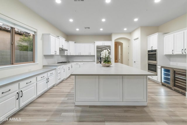 kitchen featuring white cabinets, light hardwood / wood-style flooring, beverage cooler, a kitchen island with sink, and appliances with stainless steel finishes